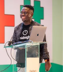 A speaker at a glass lectern with a laptop, wearing a headset microphone.